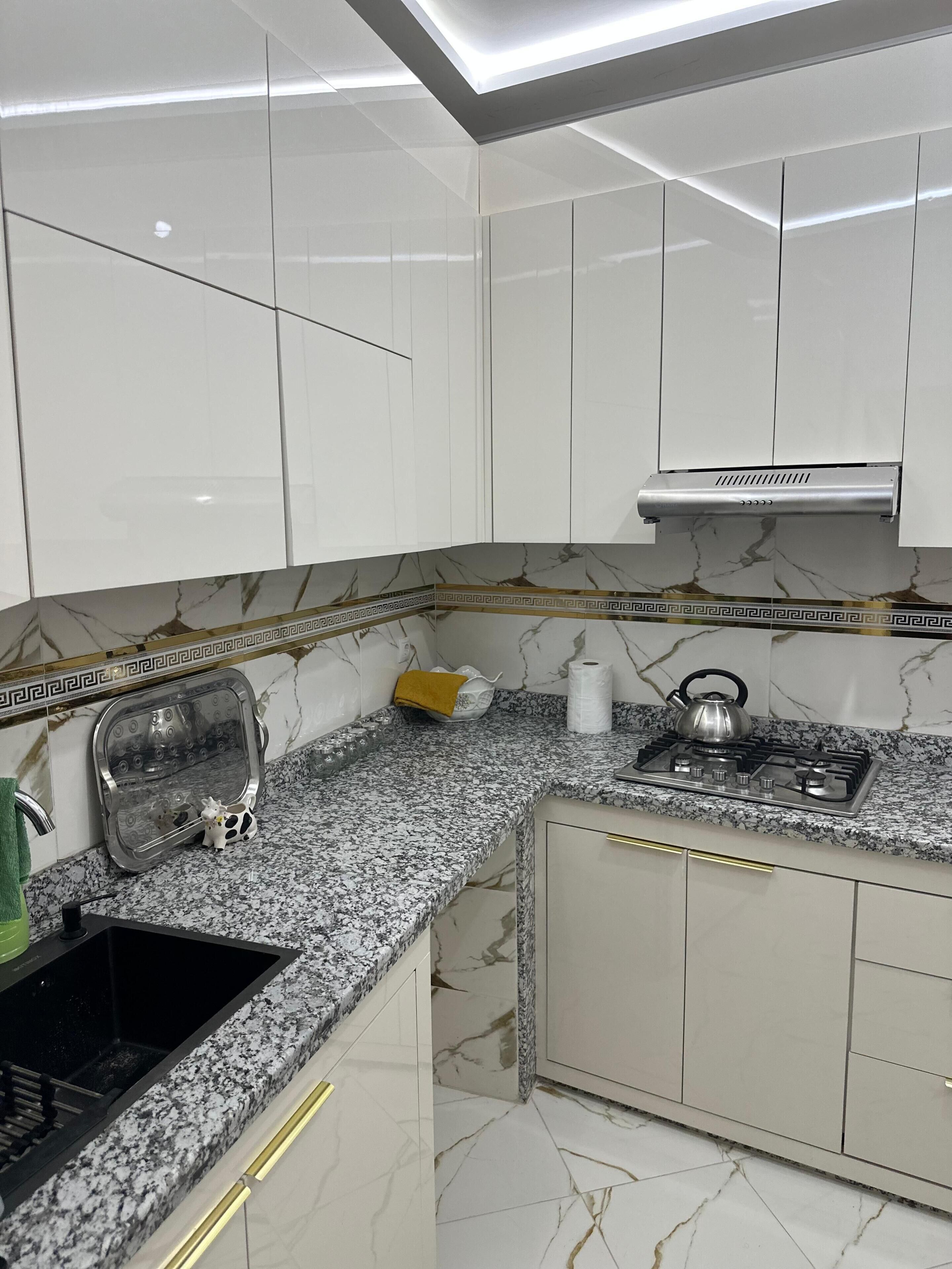 A modern kitchen with white cabinets, a granite countertop, a gas stove, and a stainless steel range hood.