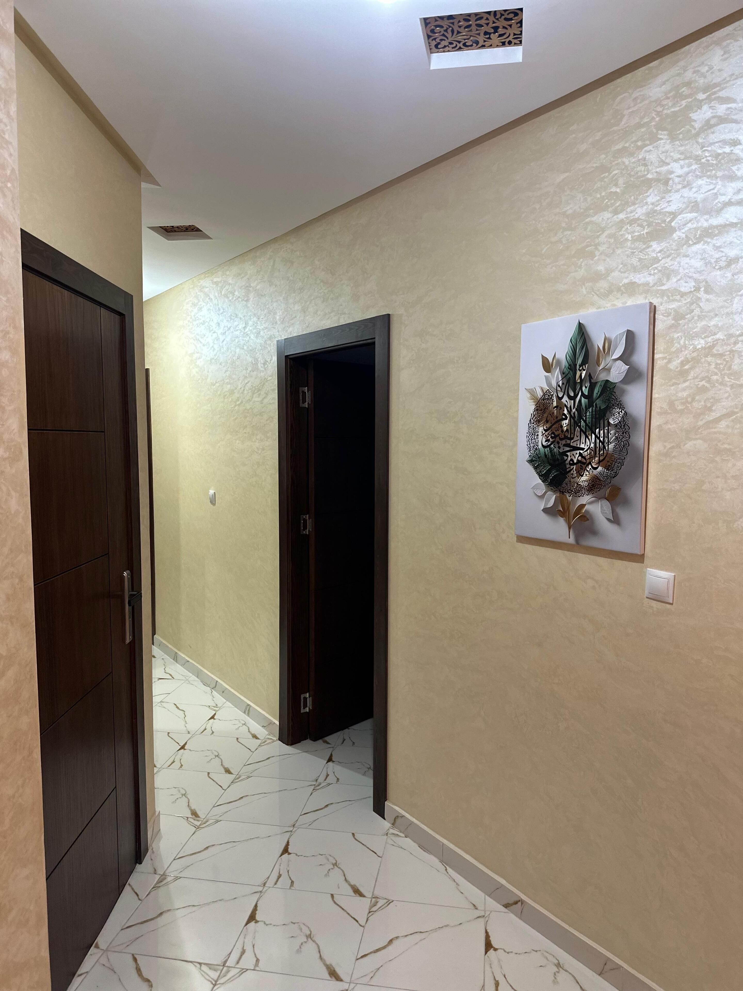 A hallway with a dark wooden door, a dark door frame, a light switch, and a wall-mounted artwork.