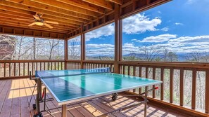 Ein Tischtennis-Tisch auf einer Holzterrasse mit Blick auf eine gebirgige Landschaft.