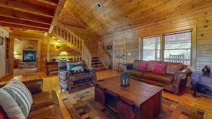A log cabin interior with a fireplace, wooden staircase, and a cozy seating area. - Moonlit Mountain Retreat | Mountain Views, Hot Tub & Fantastic Game Room (Sevierville)