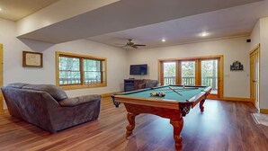 Quarto com mesa de bilhar, sofá de couro e televisão.