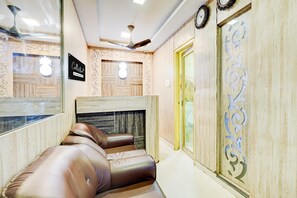 A hotel room with a seating area, a ceiling fan, a wall clock, and a door with a decorative number. - CollectionO Guduvancheri Railway Station (Chennai)