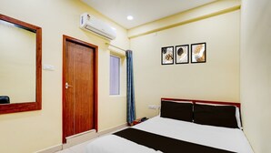 A hotel room with a bed, a door, an air conditioning unit, a window with a curtain, and three framed pictures on the wall. - CollectionO Guduvancheri Railway Station (Chennai)