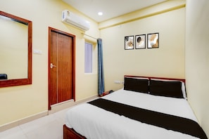 A hotel room with a bed, a door, an air conditioning unit, a window with a curtain, and three framed pictures on the wall. - CollectionO Guduvancheri Railway Station (Chennai)