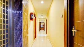 A hotel corridor with a marble wall, a wooden door, and a fire extinguisher. - CollectionO Guduvancheri Railway Station (Chennai)