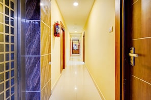 A hotel corridor with a marble wall, a wooden door, and a fire extinguisher. - CollectionO Guduvancheri Railway Station (Chennai)