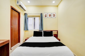 A bedroom with a bed, a window with curtains, a wall-mounted air conditioner, and three framed pictures. - CollectionO Guduvancheri Railway Station (Chennai)