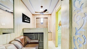 A reception area with a leather sofa, a sign indicating a company service, a ceiling fan, and a wooden wall with decorative cutouts. - CollectionO Guduvancheri Railway Station (Chennai)
