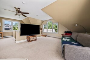 A spacious living room with a large flat-screen TV, a ceiling fan, and a view of the outdoors through large windows. - Mingo Manor | Across from Mingo Springs Golf Course!! (Rangeley)