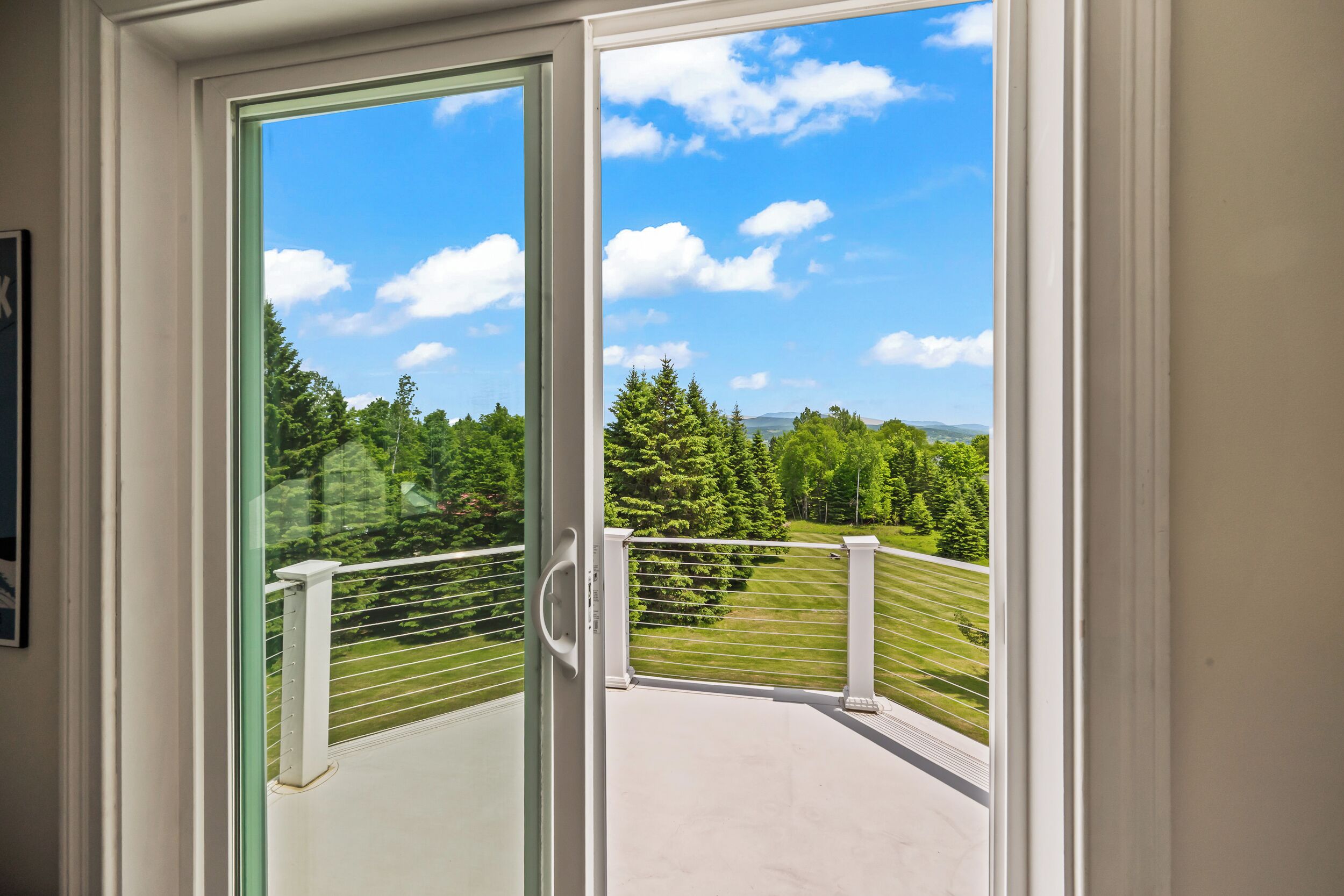 A balcony with a glass door leading to a view of a green landscape and trees.
