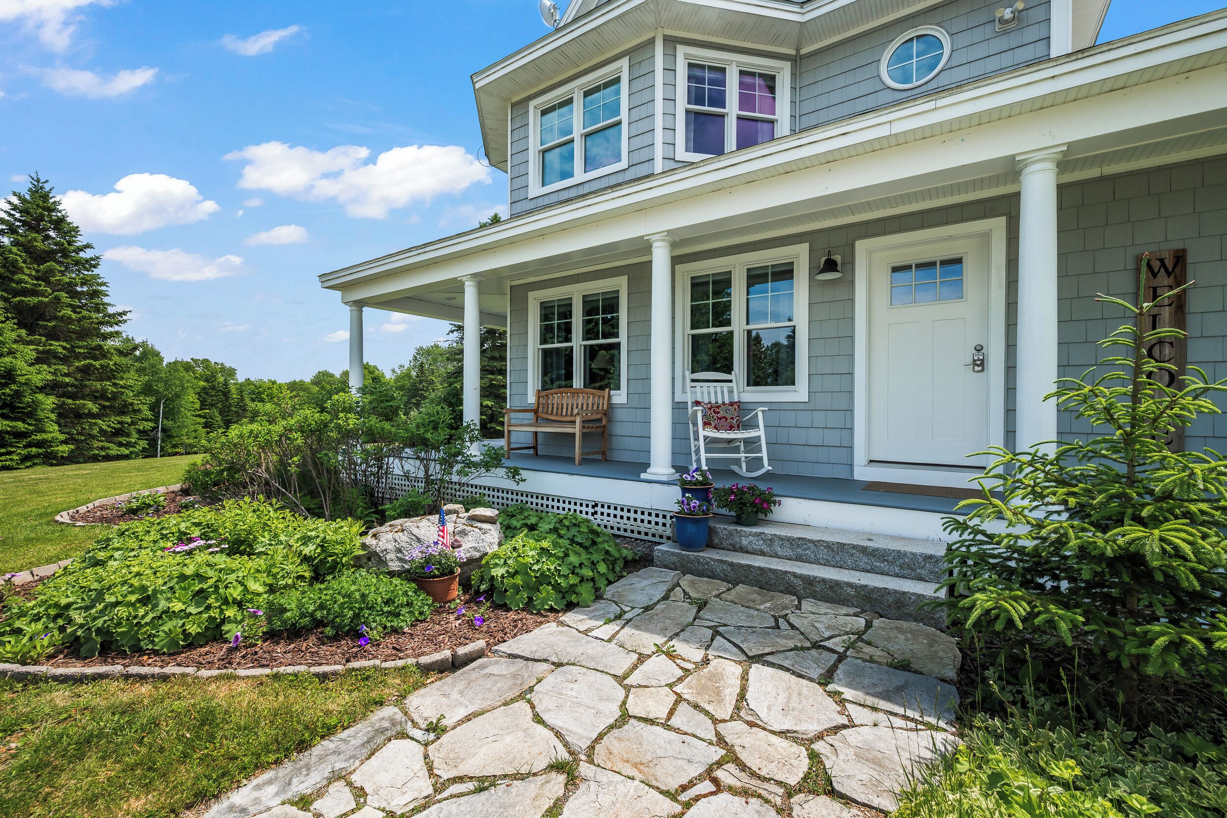 A two-story house with a covered porch, a stone pathway, and a well-maintained garden.