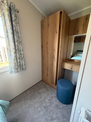 Ein Schlafzimmer mit einem Holzschrank, einem kleinen Hocker, einem Fenster mit Vorhängen und einem Bett.