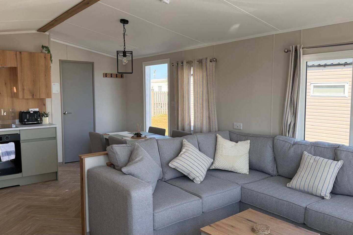 Een moderne woonkamer met een grijze bank, een houten salontafel en een keuken met een broodrooster.