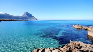 Kustlandschap met helderblauw water, rotsformaties en een berg in de verte.