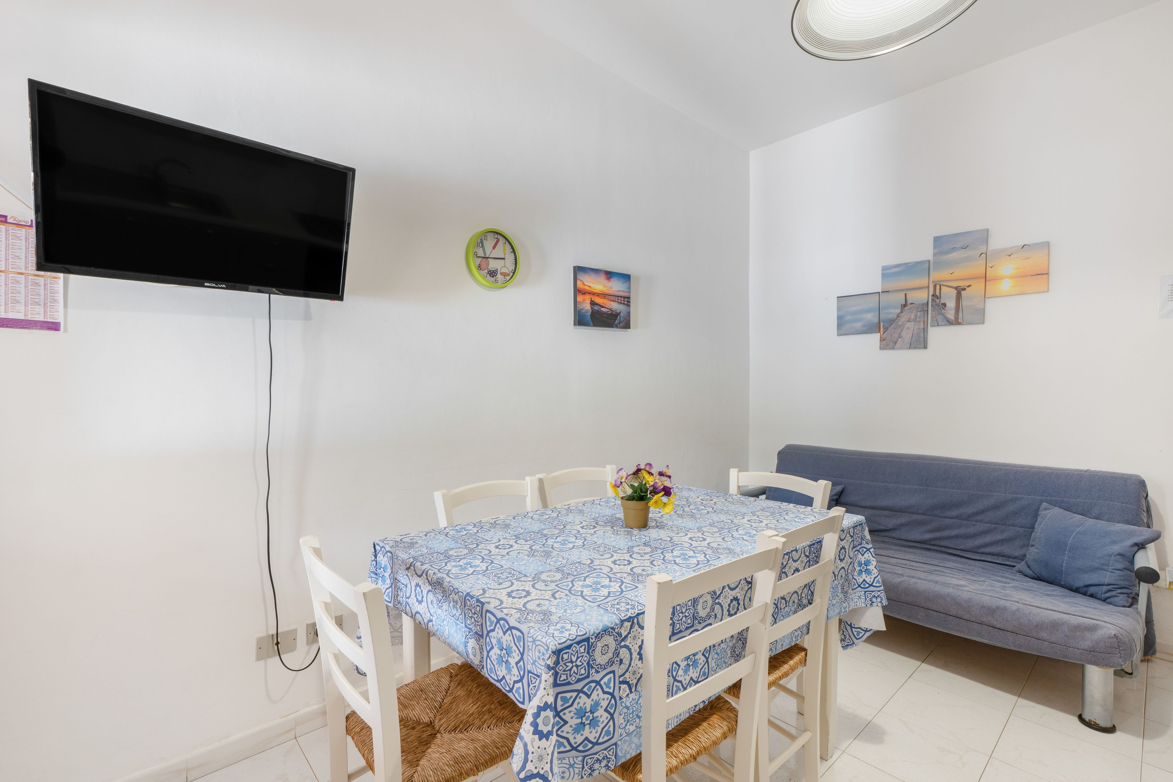 Une pièce comprenant une table à manger, des chaises, un canapé, un téléviseur à écran plat, une horloge murale et des œuvres d’art.