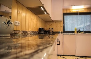 Une cuisine avec des murs en bois, un plan de travail en marbre et une fenêtre équipée de stores.