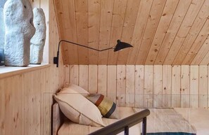 Un intérieur en bois avec un plafond incliné, une lampe noire fixée au mur et un banc rembourré agrémenté de coussins.