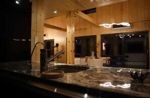 Eine Küche mit einer Granitarbeitsplatte, einer Edelstahl-Spüle und Holzwänden.