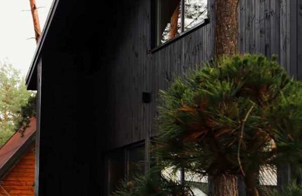 Un bâtiment moderne à l’extérieur sombre, doté de grandes fenêtres et surmonté d’un arbre en premier plan.