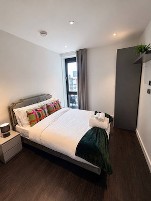 A modern hotel room with a large bed, a bedside table, a wardrobe, and a window with curtains. - Apartamento moderno a 3 min do Wembley Stadium e London Designer Outlet. (Wembley)