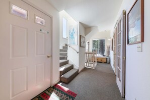A hallway with a carpeted floor, a staircase with a railing, and a door with a window. - Spike's Place at Tahoe Donner by Tahoe Getaways - 2BR w 2 Bonus Rooms & Walking Distance to HOA! (Truckee)
