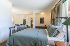 A bedroom with a bed, a bedside table, a lamp, and a window with curtains. - Spike's Place at Tahoe Donner by Tahoe Getaways - 2BR w 2 Bonus Rooms & Walking Distance to HOA! (Truckee)