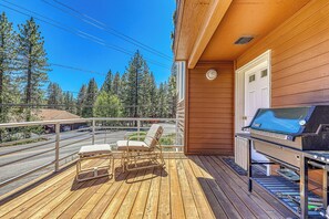 A wooden deck with two chairs and a grill, overlooking a street and trees. - Spike's Place at Tahoe Donner by Tahoe Getaways - 2BR w 2 Bonus Rooms & Walking Distance to HOA! (Truckee)