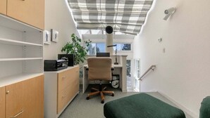 Een kleine kamer met een bureau, stoel en wandplanken.