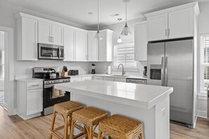 A modern kitchen with white cabinetry, stainless steel appliances, a central island with bar stools, and pendant lighting. - Hang Ten House 2.5 Blocks to Beach Pet Friendly (Myrtle Beach)