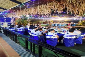 A dining area with tables and chairs, a railing, and a covered section with hanging decorations. - Dalux Motel (Banan)