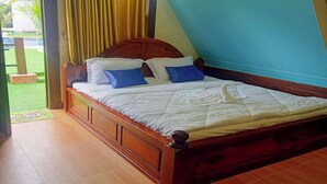 A bedroom with a wooden bed, two pillows, a blue wall, and a door leading to a garden. - Dalux Motel (Banan)