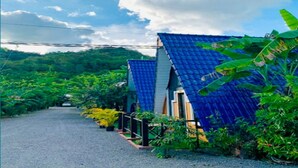 A row of blue-roofed houses with a gravel path leading through a lush green area. - Dalux Motel (Banan)