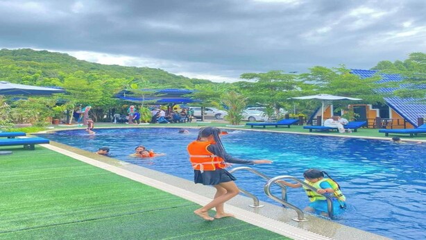A swimming pool with a lifeguard, a child in a life jacket, and people in the water. - Dalux Motel (Banan)