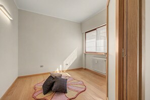 Ein Zimmer mit Holzboden, Heizkörper, einem Fenster mit Jalousien und einer Tür.