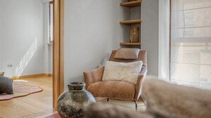 A room with a wooden floor, a chair with a cushion, a shelf with decorative items, and a large window. - Aluméa – Charming and Wellness Retreat in Central Aosta with Mountain Views (Aosta)