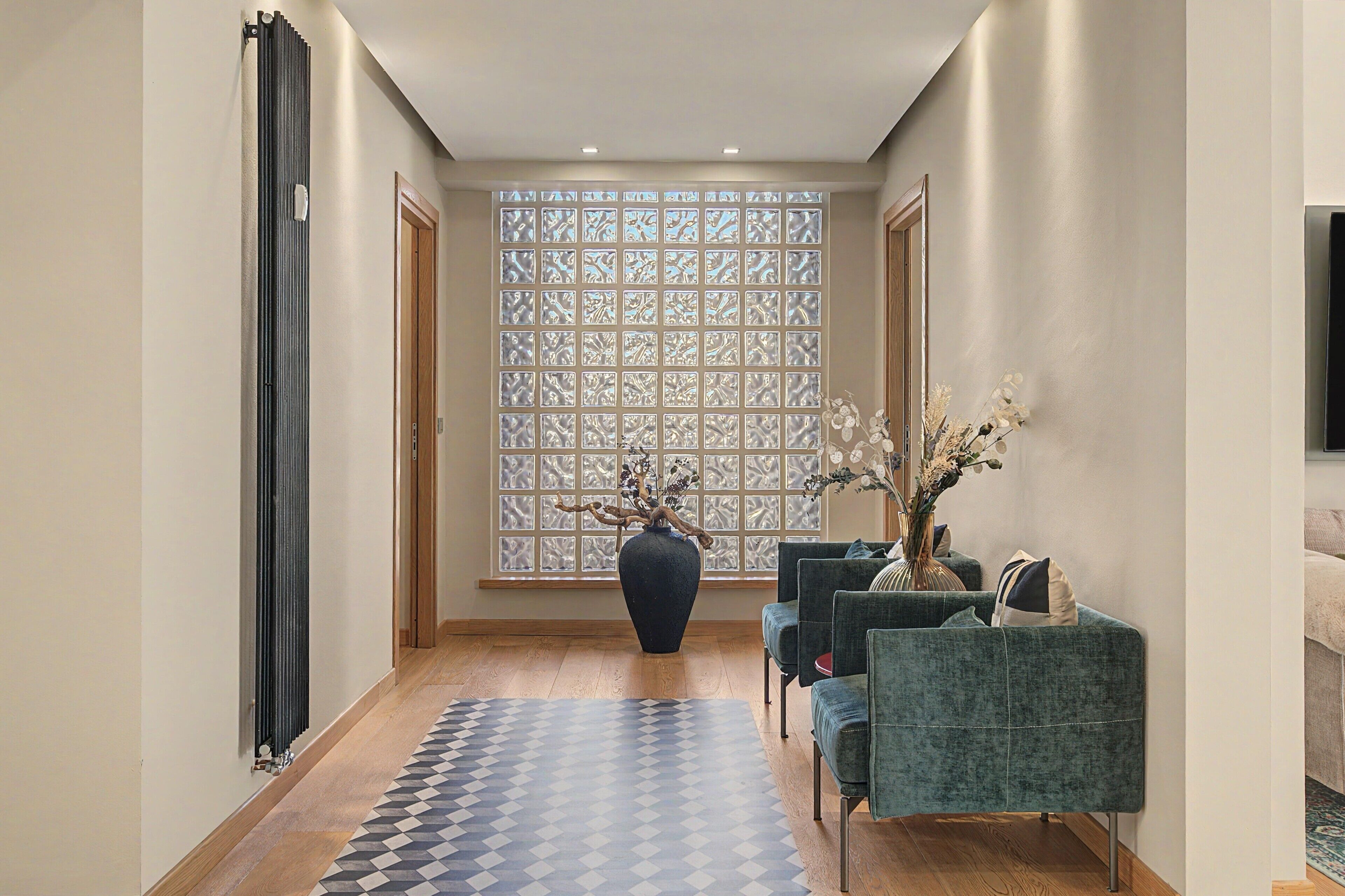Ein modernes Interieur mit einem gemusterten Boden, einer großen Vase mit Zweigen und einer Sitzecke mit gepolsterten Stühlen.