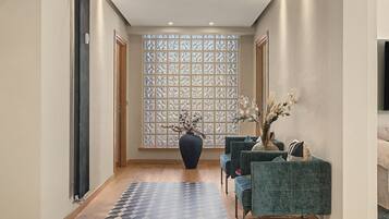 Ein modernes Interieur mit einem gemusterten Boden, einer großen Vase mit Zweigen und einer Sitzecke mit gepolsterten Stühlen.