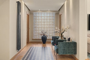 A modern interior with a patterned floor, a large vase with branches, and a seating area with upholstered chairs.