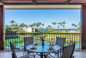 A round table with chairs and a vase, set on a balcony with a view of a golf course and ocean. - Upgraded Oceanfront Condo at Mauna Lani Terrace (Kamuela)