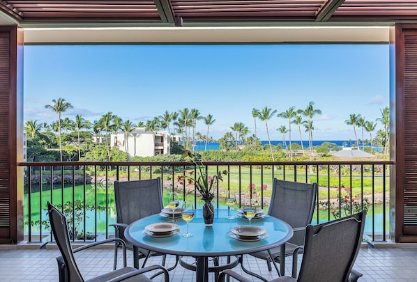 Ein runder Tisch mit Stühlen und einer Vase, auf einem Balkon mit Blick auf einen Golfplatz und das Meer.