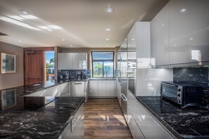 A modern kitchen with a wooden floor, black marble countertops, and stainless steel appliances. - Upgraded Oceanfront Condo at Mauna Lani Terrace (Kamuela)