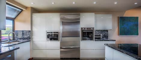 Une cuisine moderne avec des meubles blancs, des appareils en acier inoxydable et un plan de travail en marbre noir.