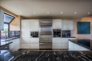A modern kitchen with white cabinets, stainless steel appliances, and a black marble countertop. - Upgraded Oceanfront Condo at Mauna Lani Terrace (Kamuela)