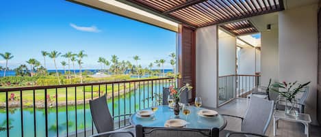 A balcony with a table set for two, overlooking a pool and palm trees.