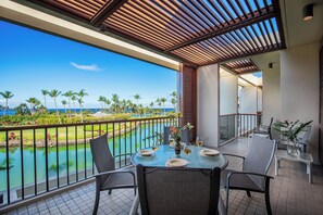 Ein Balkon mit Tisch für zwei Personen, Blick auf Pool und Palmen.