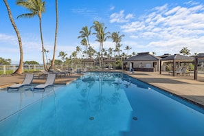 A swimming pool with lounge chairs, palm trees, and a covered area with a view of the ocean. - Upgraded Oceanfront Condo at Mauna Lani Terrace (Kamuela)