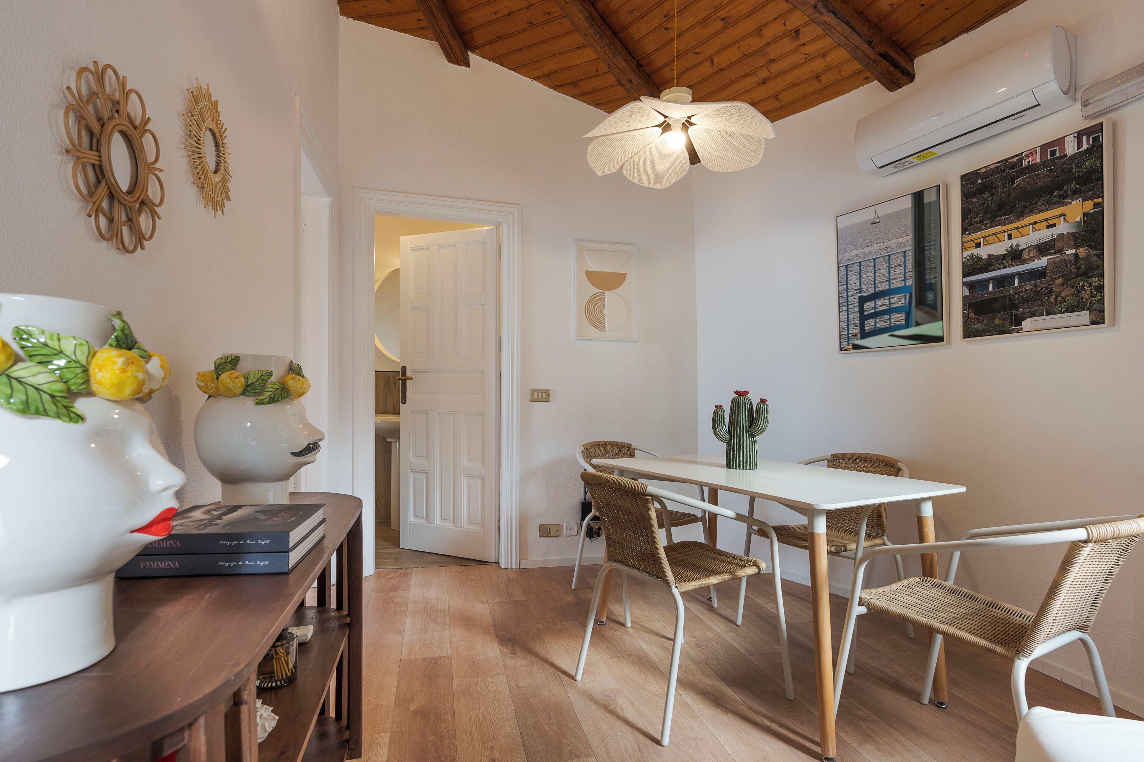 A dining area with a white table and wicker chairs, a ceiling fan, and a wall-mounted air conditioner.