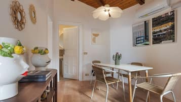 A dining area with a white table and wicker chairs, a ceiling fan, and a wall-mounted air conditioner.