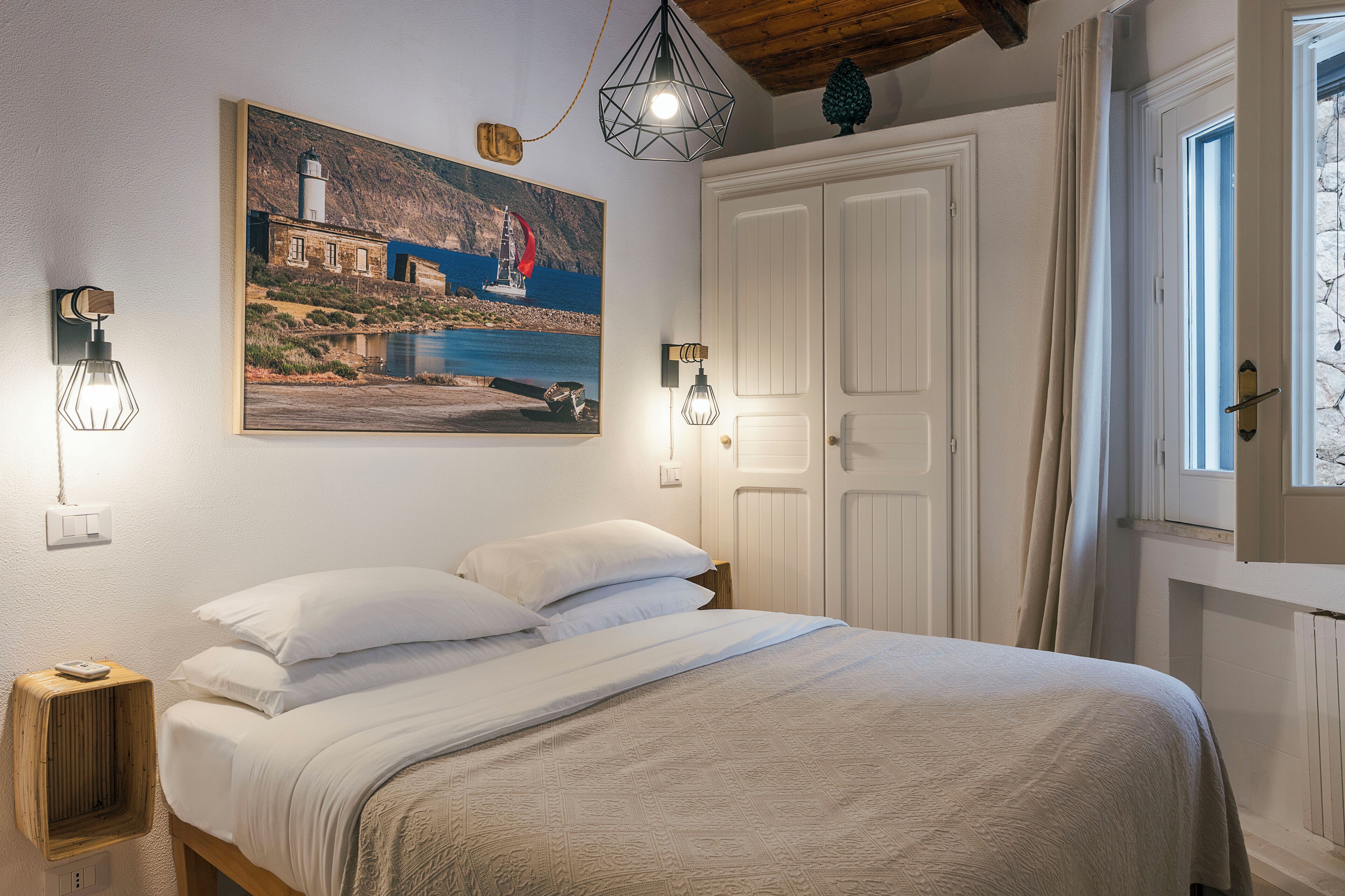 Un dormitorio con una cama, un cuadro de una escena costera y dos luces fijadas a la pared.