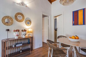 Un comedor con una mesa redonda, sillas de mimbre, un aparador de madera con adornos y espejos en la pared.